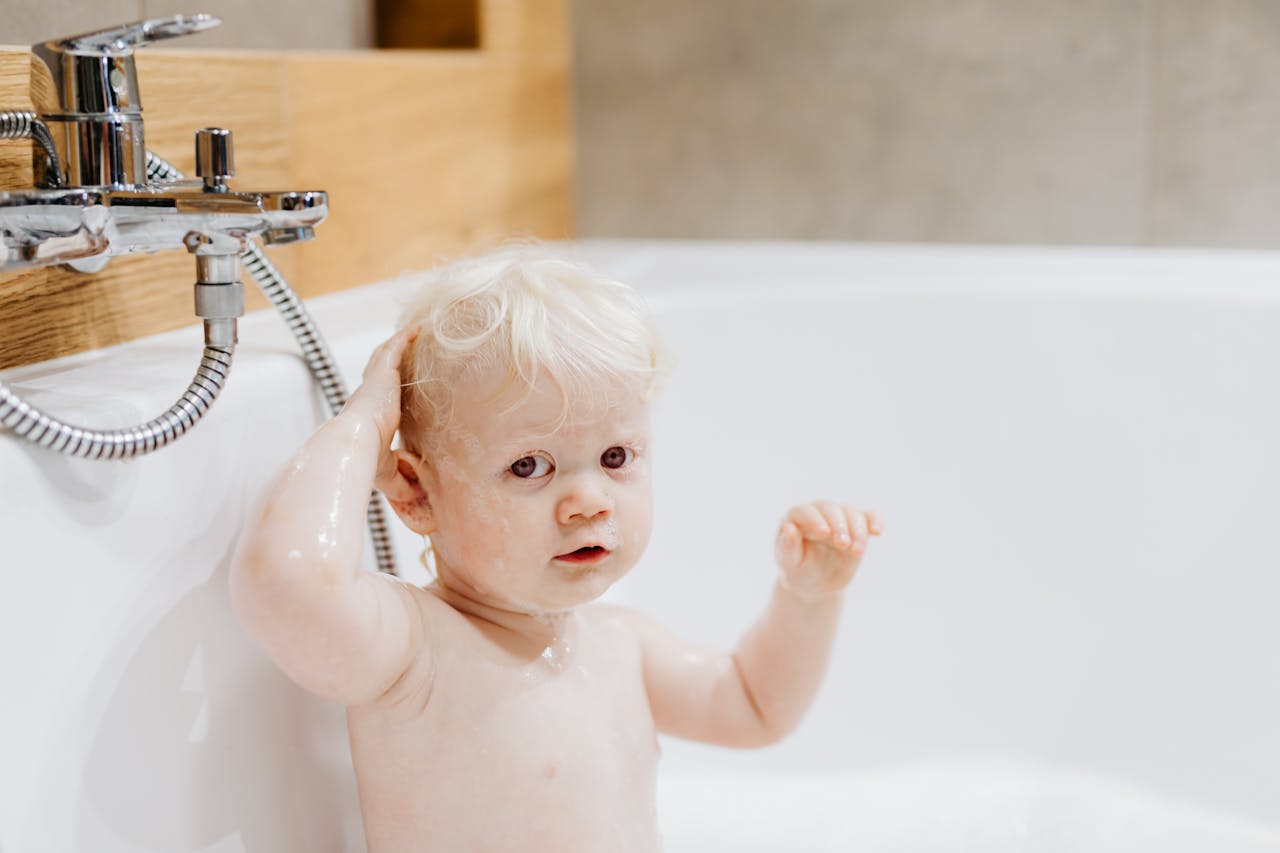 about-02 Cute toddler with blonde hair enjoying bath time with bubbles in a cozy bathroom.
