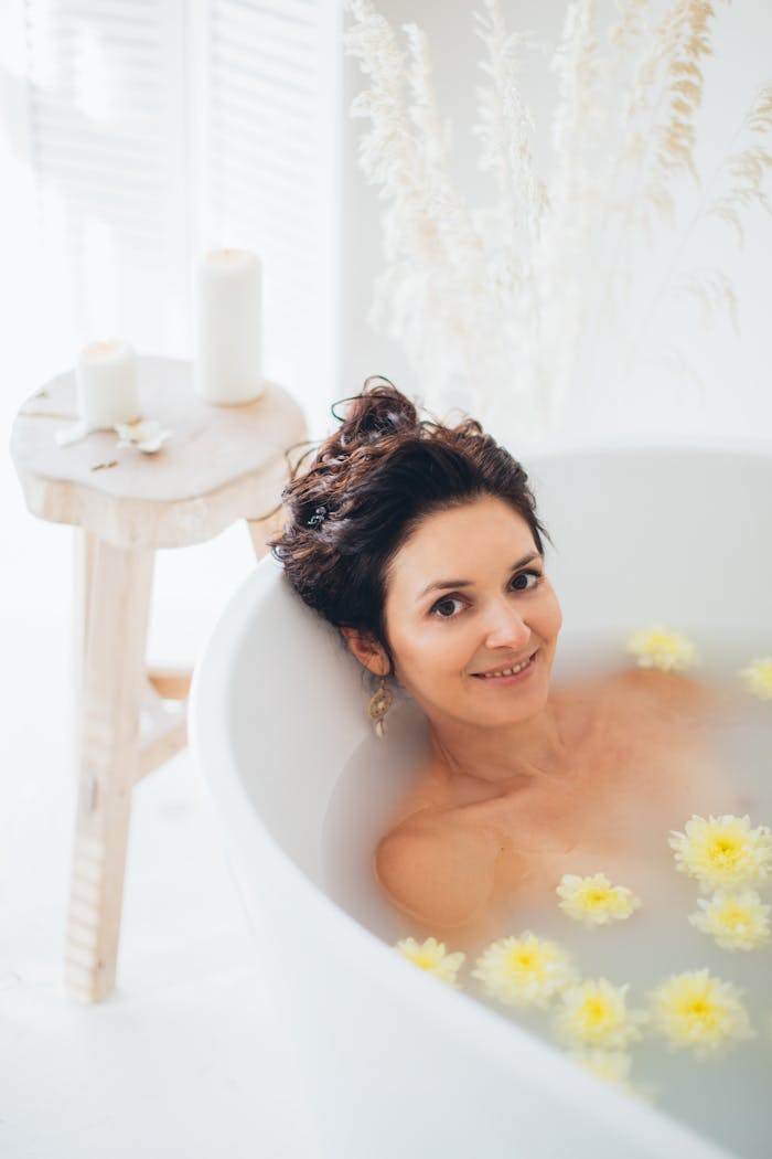 about-01 A woman relaxing in a milk bath with floating flowers, creating a peaceful and serene spa atmosphere.